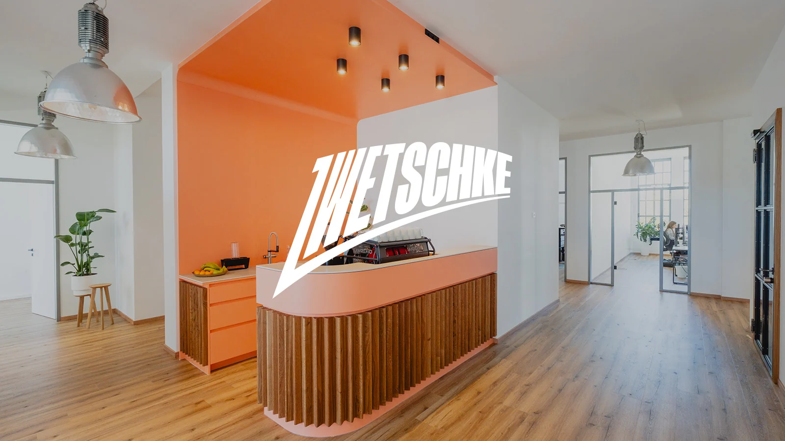 Empfang im zwetschke-Büro in Augsburg: Theke mit Kaffeemaschine unter koralle Decke, darüber die zwetschke-Wortmarke