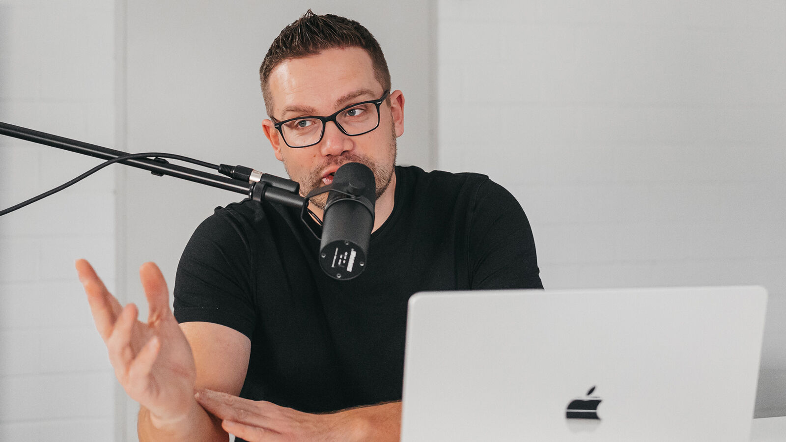 Ein Mitarbeiter von hearwego spricht am Studiomikrofon und gestikuliert, vor sich ein Laptop.