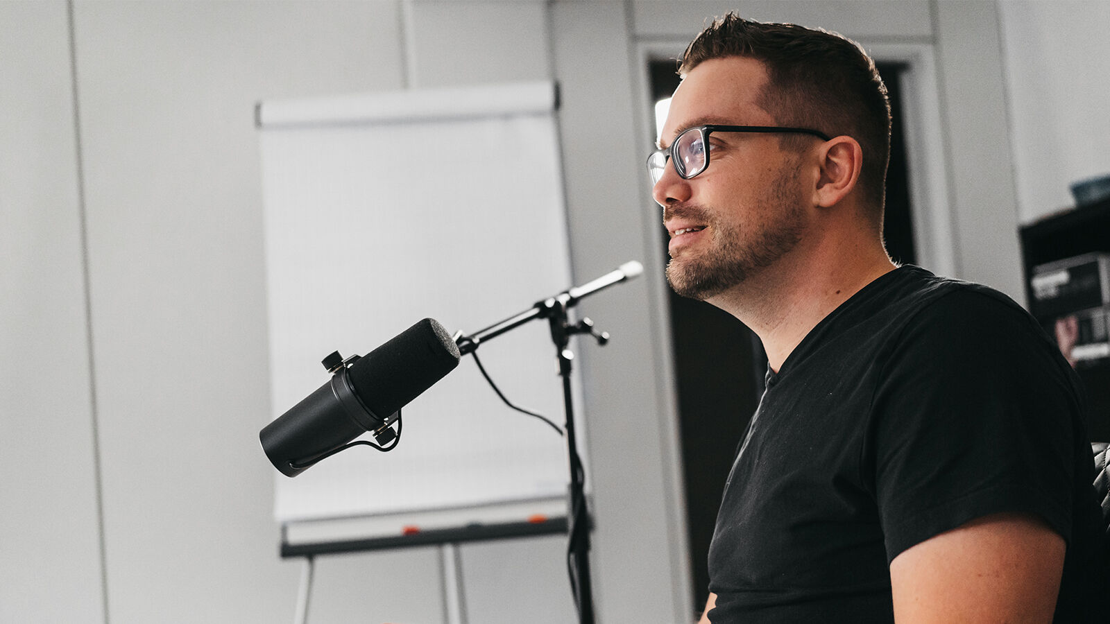 Ein Mitarbeiter von hearwego im Profil am Studiomikrofon, im Hintergrund ein Flipchart.