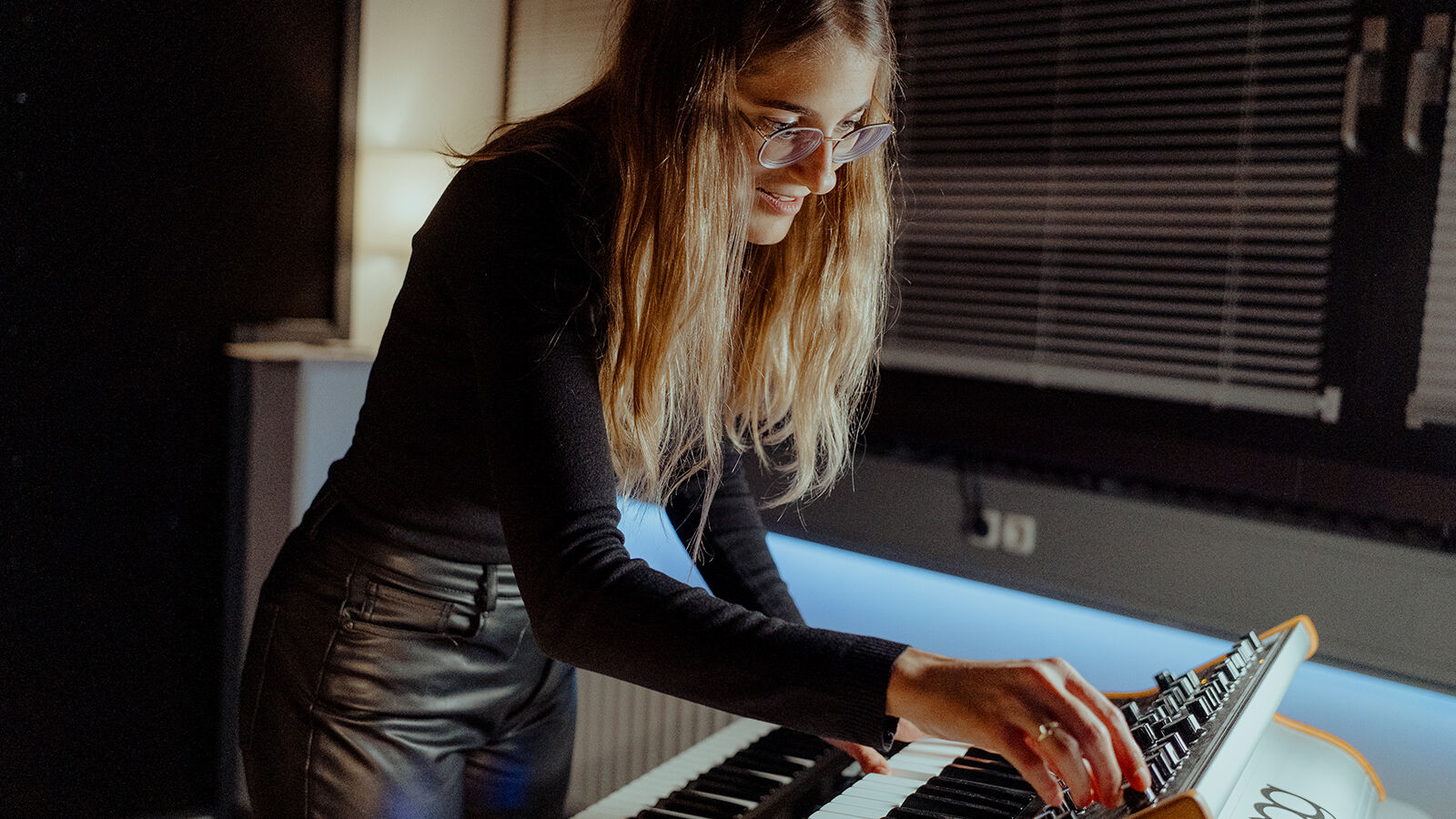 Eine Mitarbeiterin von hearwego spielt im abgedunkelten Studio an einem Synthesizer.