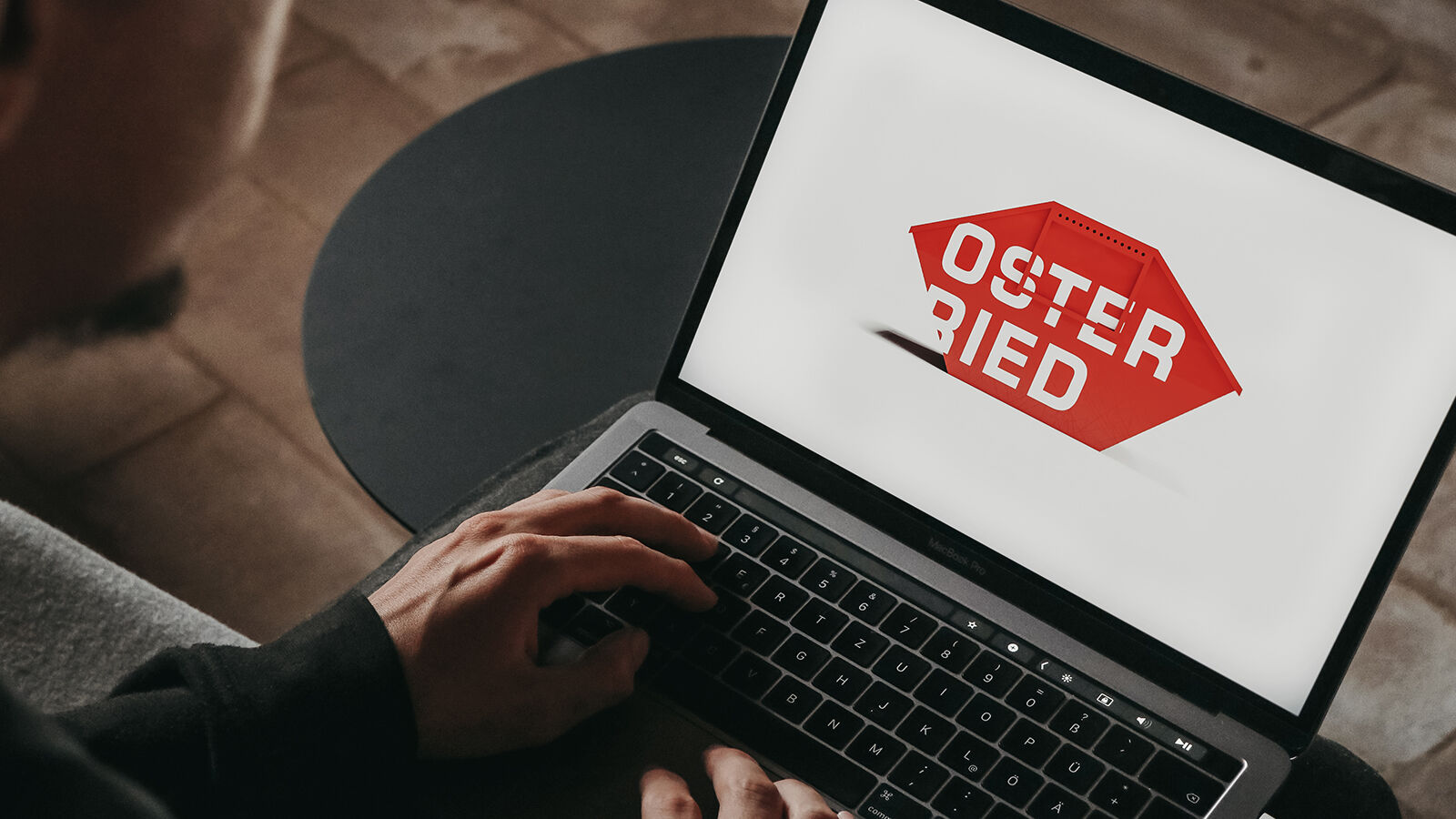Blick über die Schulter auf einen Laptop, auf dem das rote Osterried-Hauslogo steht.